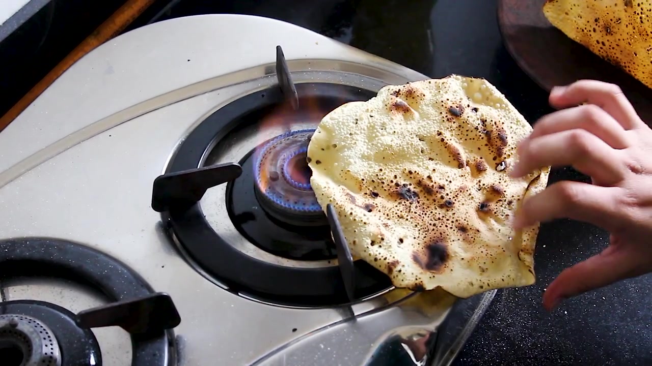 Papad tenuto su fiamma a gas aperta fino a renderlo croccante, primo piano in una cucina indiana. Ideale per contenuti alimentari, tutorial di cucina e B-roll culinari autentici