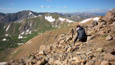 female photographer sitting on edge of slope taking picture of colorado rocky mountains during the winter, handheld