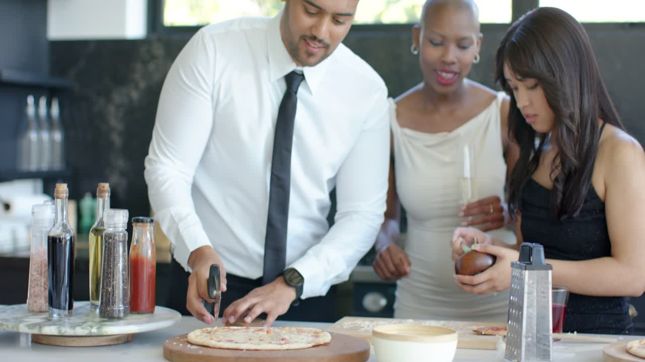 Diverse friends around man in tie placing, cutting pizza, ladling batter, serving at kitchen island