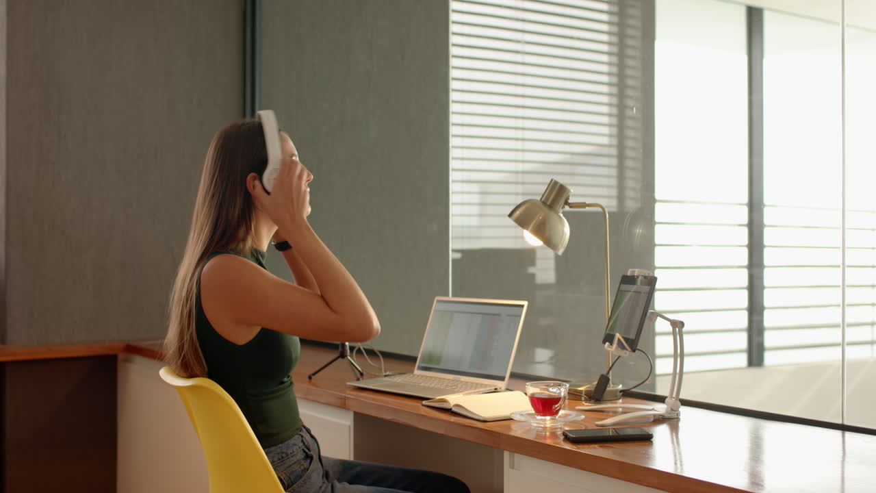 Talking on smartphone, woman working on laptop at home office desk
