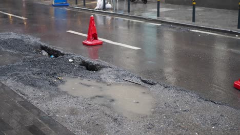 a large pothole in a city street, filled with water and surrounded by a traffic cone