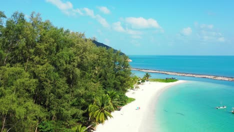 Peaceful-exotic-beach-with-beautiful-palm-trees-bent-over-white-sand-washed-by-calm-turquoise-lagoon-on-a-bright-blue-sky-background