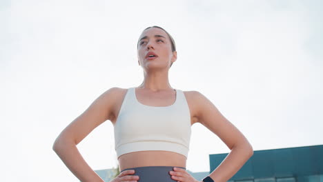 young caucasia female runner is short of breath after a fast sprint run in urban city park sunny day