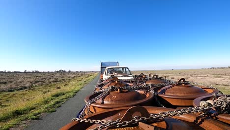 Shot-taken-from-the-top-of-a-truckload,-landscape-with-low-vegetation-and-blue-sky-with-clouds-on-the-horizon