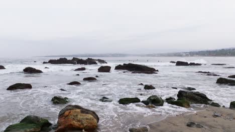 Establishing-dolly-over-rocks-in-shallow-sandy-waters-to-surfers-on-horizon-in-Puerto-Escondido-Oaxaca-Mexico