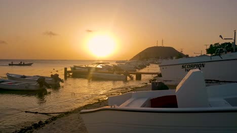 Orange-sunset-beach-with-fishing-pier,-sea-birds-and-motorboats-in-tropical-island