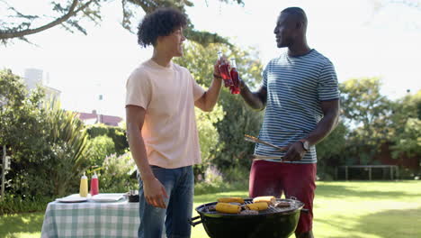 grilling corn on barbecue, two multiracial male friends drinking soda and enjoying outdoor hangout