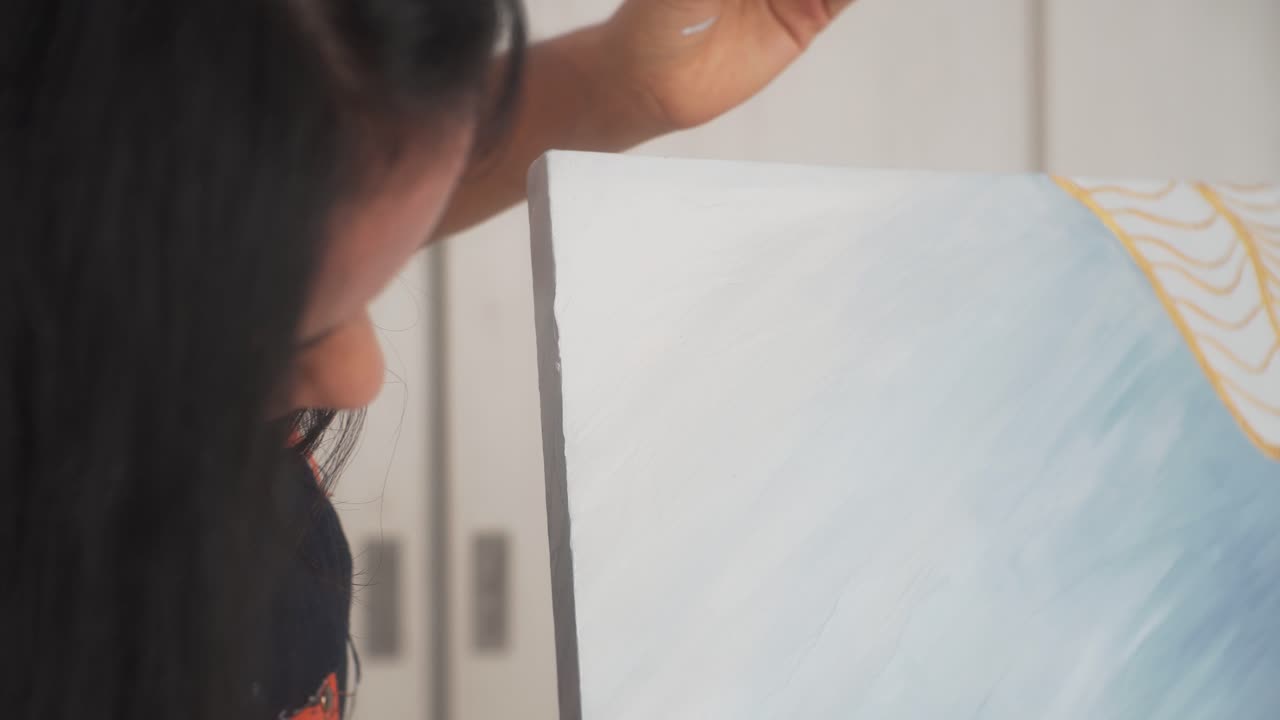 여성 예술가는 추상 오일 작품의 캔버스 측면을 조심스럽게 칠합니다.