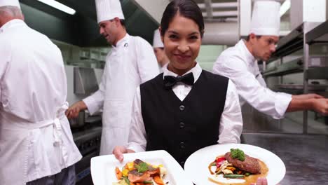 Smiling-waitress-showing-two-dishes-to-camera