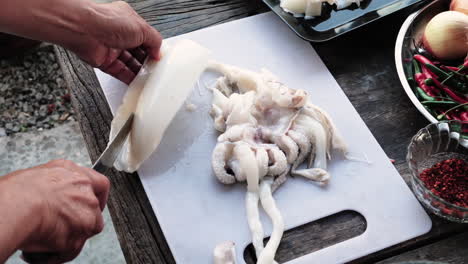 las manos del chef limpiando y recortando calamares, ingredientes para la preparación de alimentos en la mesa
