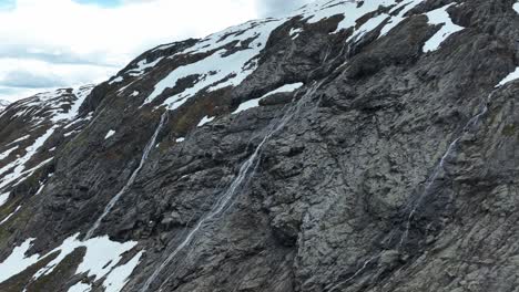 Snow-covered-rocky-mountain-with-cascading-waterfalls-in-Norway