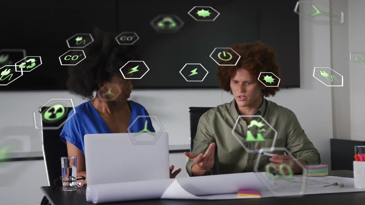 Woman gesturing and man holding pen starting energy meeting, green AR icons overlaying laptop plans