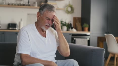 Älterer-Kaukasischer-Mann-Mit-Kopfschmerzen,-Der-Zu-Hause-Auf-Der-Couch-Sitzt.