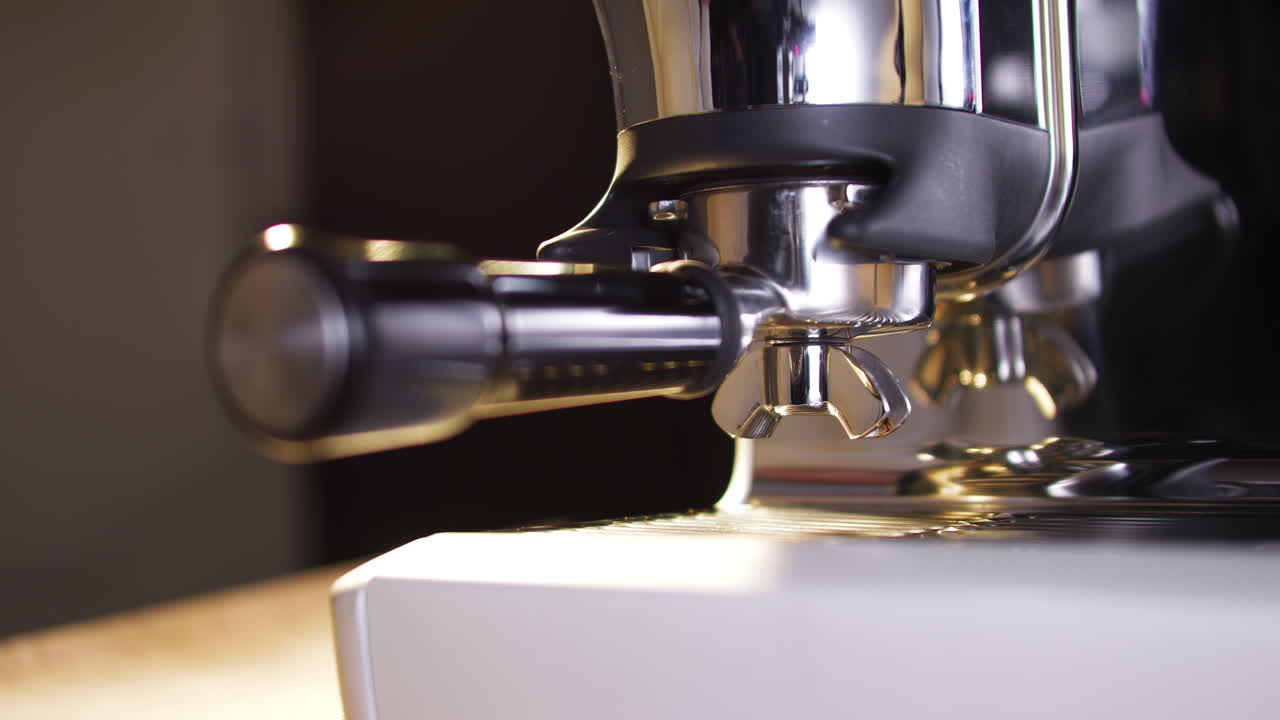 Uma mão insere um portafiltro no encaixe do moedor de uma elegante máquina de café expresso de aço inoxidável. O close-up destaca o momento de preparo em um ambiente premium, suavemente iluminado para fazer café.