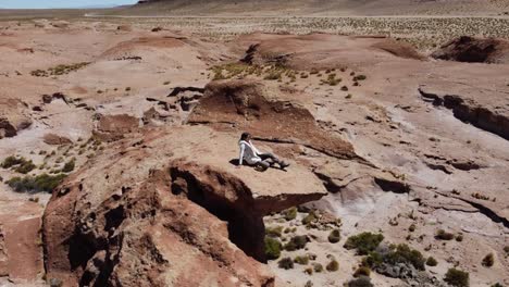 Aerial-orbits-woman-on-high-rock-spire-in-barren-altiplano,-Bolivia