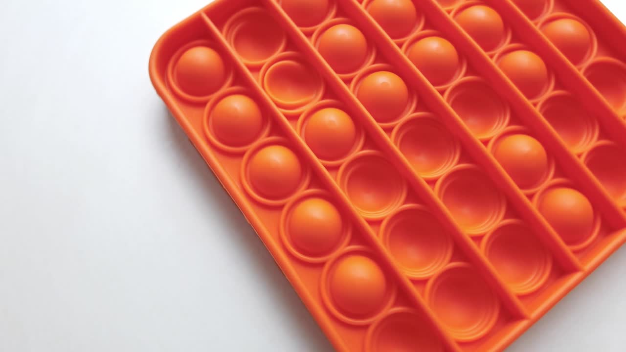 nuevo juguete para bebés. pop it juego de dedos. color gracioso. colorido juego girar en la mesa blanca. cuadrado naranja