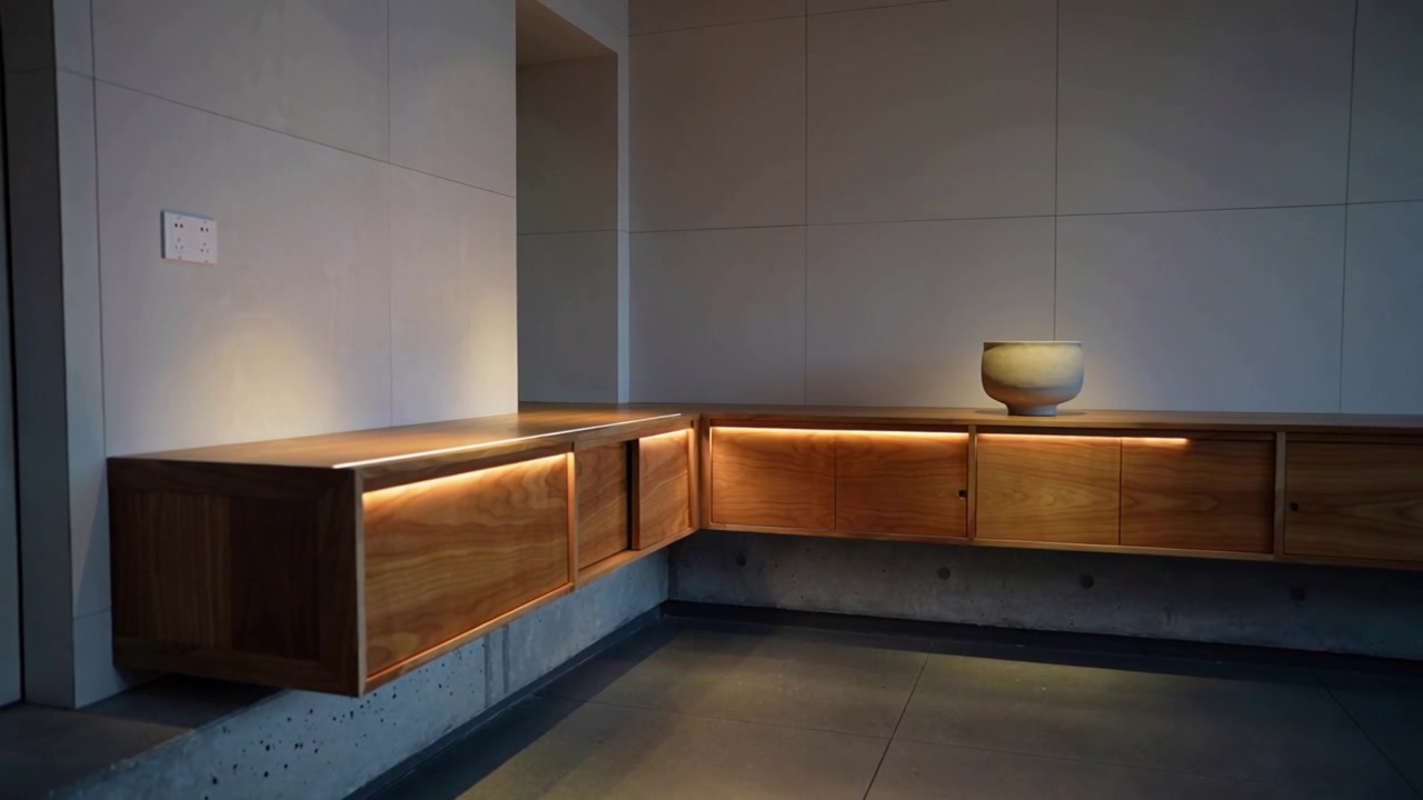 Panoramica della telecamera verso destra che rivela un mobile in legno a forma di L nell'ingresso, mostrando una calda luce LED e una ciotola.
