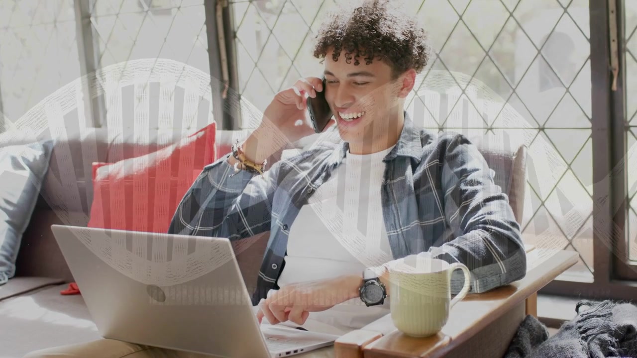 Man sitting on couch taking call while tapping laptop, window light casting stripes, working remote