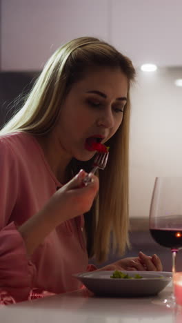 stylish woman eats salad of fresh vegetables sitting at elegant served table with gentle flowers bouquet and aromatic candle in kitchen slow motion