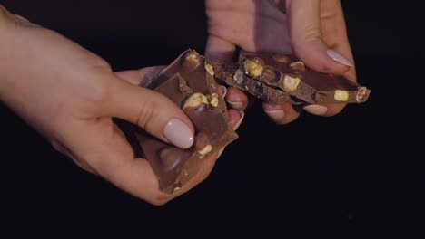 woman breaks black chocolate bar with nuts. close-up. slow motion