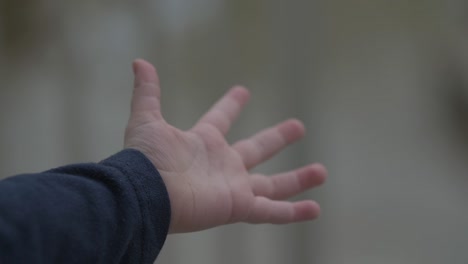 The-hand-of-a-young-boy,-child,-toddler-playing-in-the-rain-catching-rain-drops-in-his-hands-in-cinematic-slow-motion