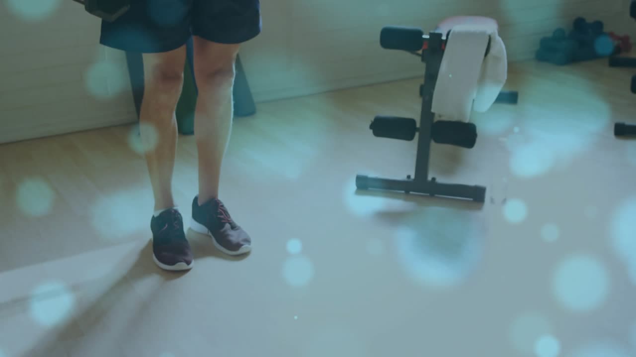 Man doing weighted lunges in gym, stepping, starting blue bokeh over him and dumbbells for fitness
