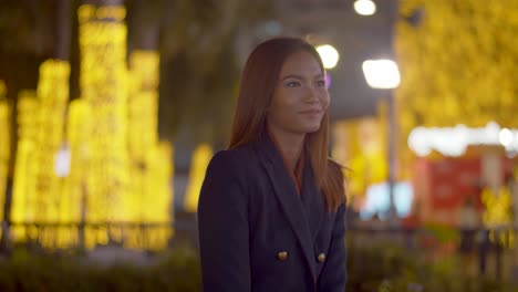 attractive woman under the bright city lights at night smiles at the camera - static with background blur