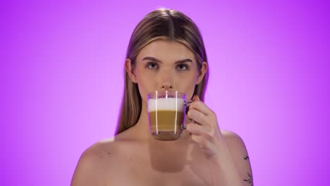 Medium-close-up-shot-of-a-young-pretty-woman-or-model-enjoying-her-morning-fresh-brewed-vegan-latte-macciato-or-cappuccino-coffee-in-front-of-purple-background-in-slow-motion