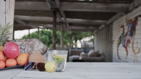 sunglasses, drink and fruits on counter at beach bar, in slow motion with copy space