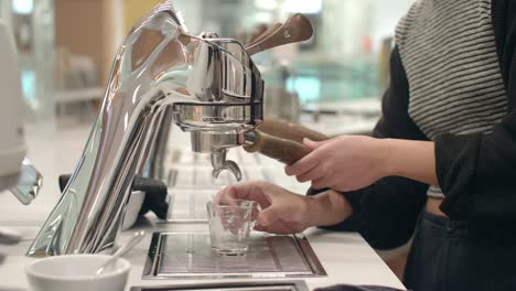 female cafe worker sets portafilter in espresso machine, places glass cup below