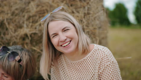 happy woman laughing joyfully with friend smiling beside her near hay bale, surrounded by vast farmland, bright outdoor setting captures cheerful moment filled with happiness