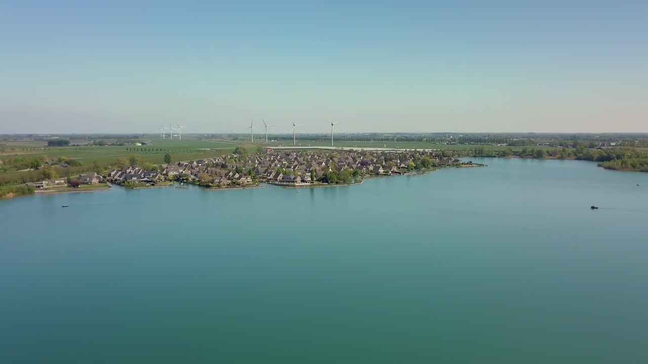 Aerial drone shot of panning to the left on the lake revealing the suburban and flat landscape with windmills in the Netherlands.