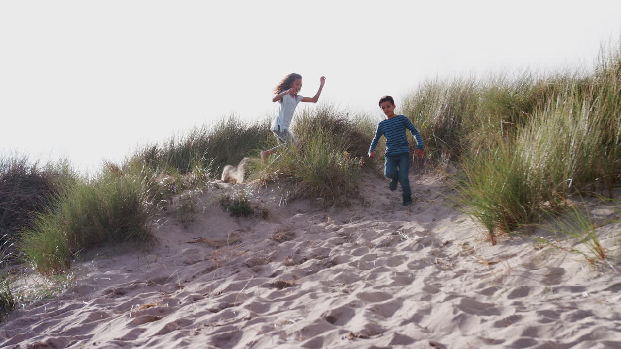 Due bambini che corrono e saltano sulle dune di sabbia in vacanza invernale al mare