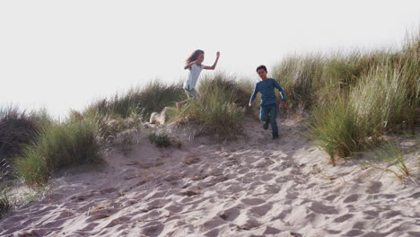 Two-Children-Running-And-Jumping-In-Sand-Dunes-On-Winter-Beach-Vacation