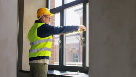 Männlicher-Baumeister-Mit-Lineal-Und-Klemmbrett,-Das-Fenster-Misst.-Baugeschäft-Und-Gebäudekonzept.-Männlicher-Baumeister-Mit-Lineal-Und-Klemmbrett,-Das-Fenster-Misst.