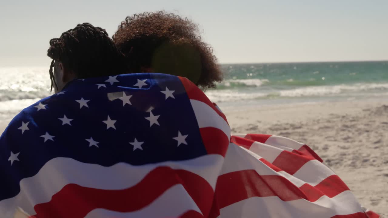 pareja envuelta en bandera estadounidense sentada juntos en la playa 4k