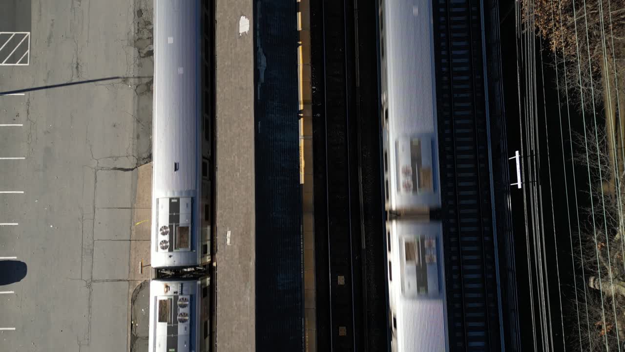 A top down view directly over a train station platform as two trains arrive on a sunny day