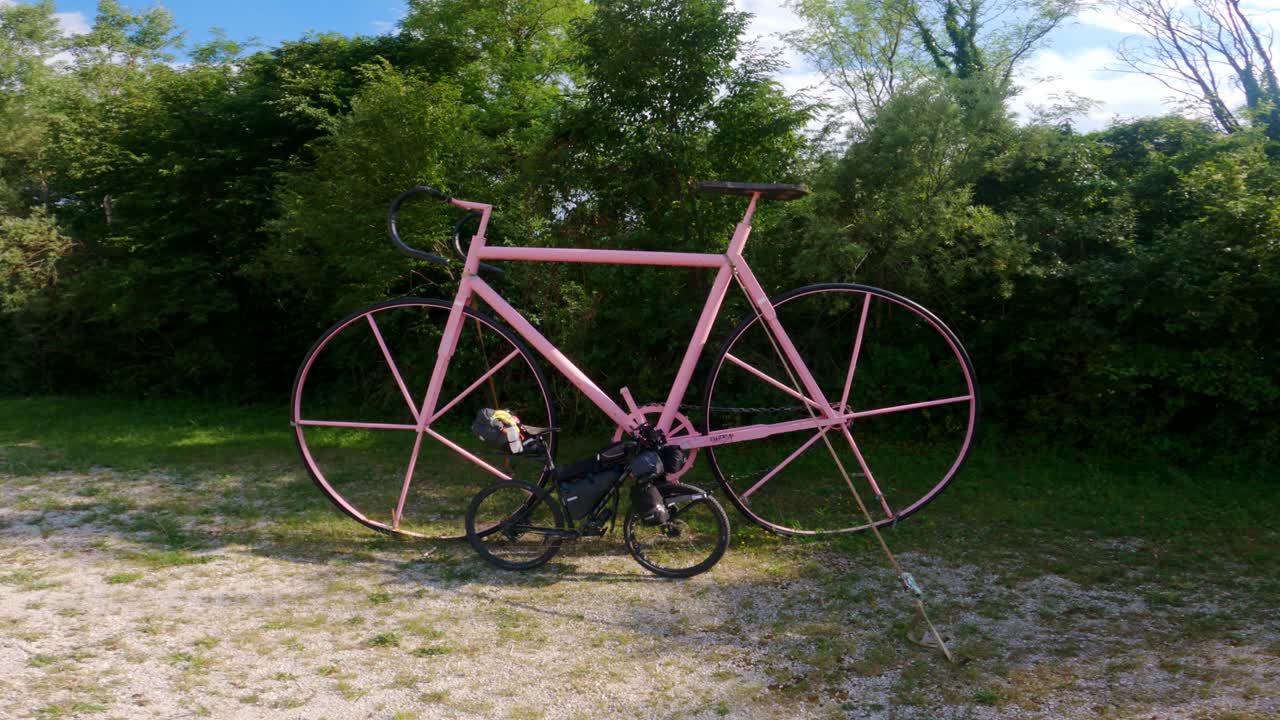 A giant pink bicycle sculpture with a black bikepacking bicycle parked beside it