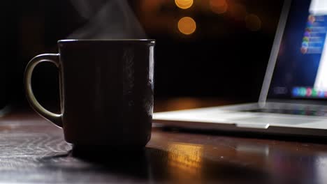 a warm cup of coffee steams gently beside a laptop, creating a cozy and inviting work space or cafe atmosphere for productivity and relaxation