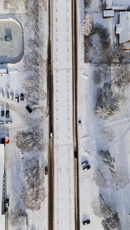 Vertical drone shot above traffic on snowy city streets, sunny, winter day