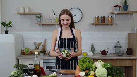 Smiling-young-girl-eating-fresh-raw-vegetable-salad-posing-at-kitchen-having-positive-emotion