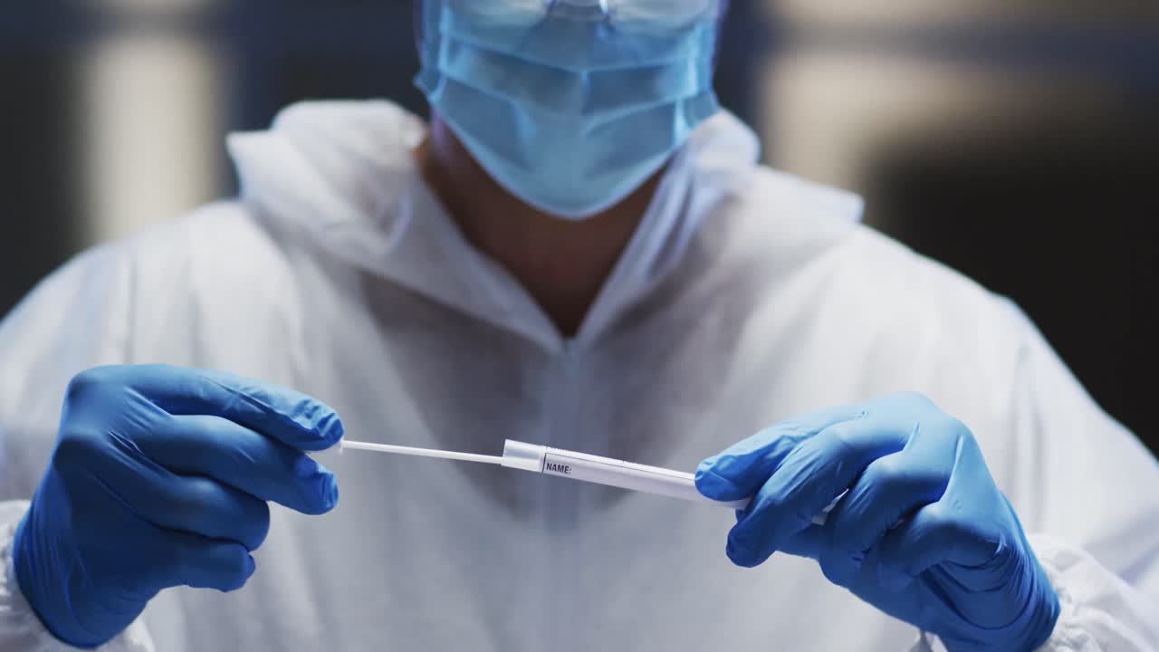 Medical worker in protective clothing and face mask examining patient swab test