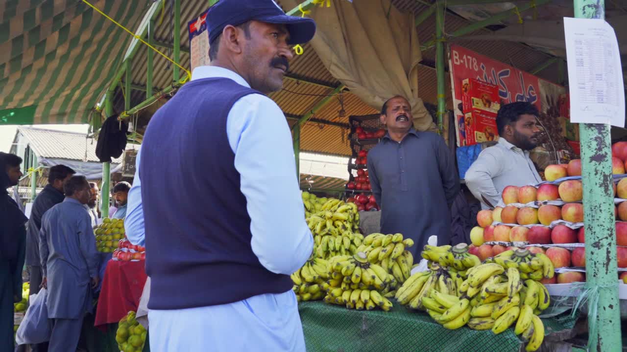Fresh fruit market in Islamabad Pakistan is teeming with people busily selecting and purchasing fruits from abundant displays.