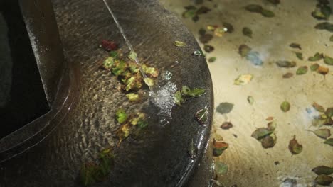 Nahaufnahme-Des-Wassers,-Das-Aus-Einem-Kleinen-Brunnen-Fließt,-Mit-Herbstblättern-Am-Boden