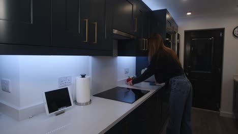 Female-model-wiping-down-a-white-quartz-worktop-by-a-induction-cooker-top-in-a-kitchen