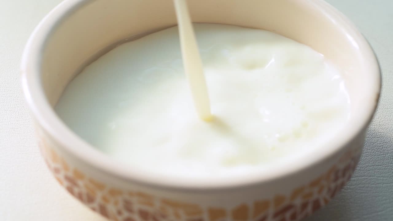 Milk being poured into a empty beautiful white bowl. Pouring milk and splashing. Slow.