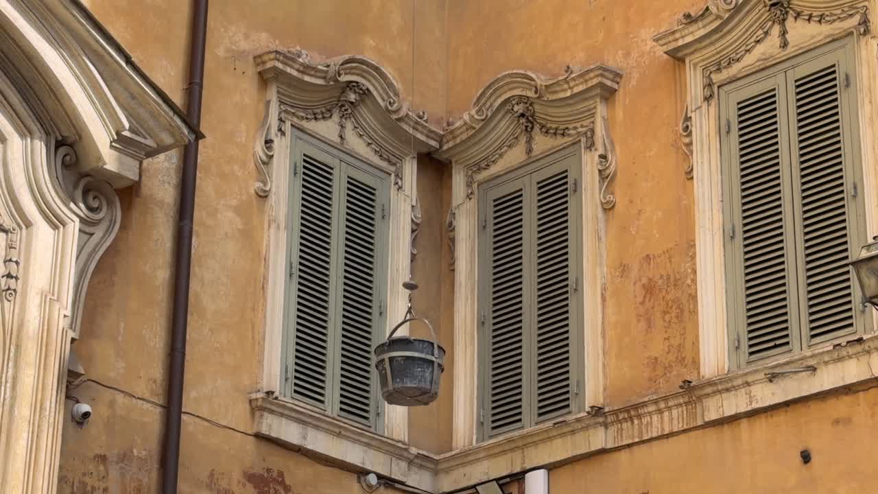Secchio calato tra finestre ornate di un vecchio edificio.