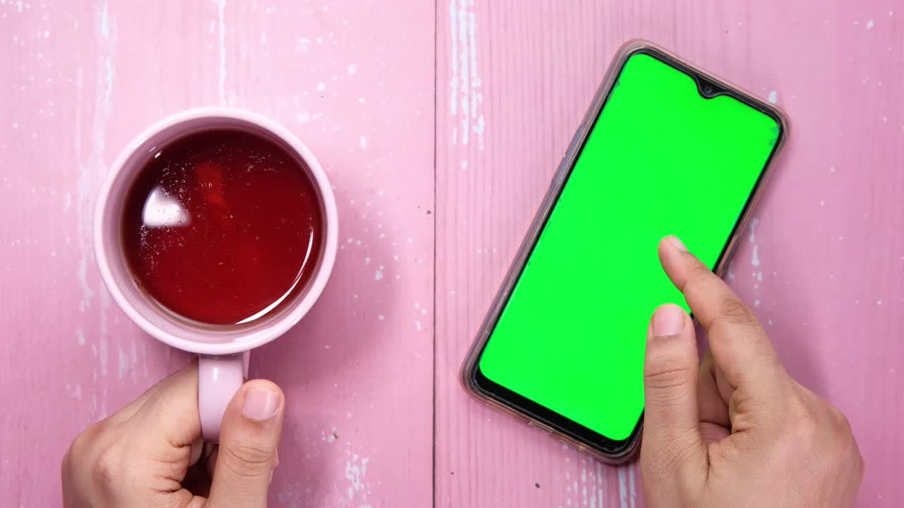 teléfono inteligente con pantalla verde y taza de té en una mesa rosa
