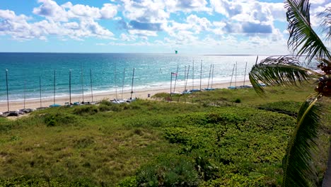 A-beautiful-drone-shot-flying-the-coast-of-Delray-Beach,-FL-with-hobie-cat-sailboats-and-a-kite-surfer