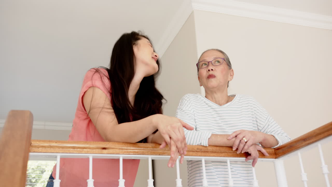 Talking and leaning on railing, Asian grandmother and granddaughter enjoying conversation at home